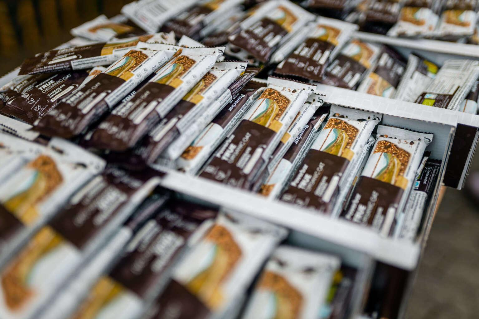 Numerosas barritas energéticas en envases de plástico blanco-marrón y almacenadas en cajas de cartón